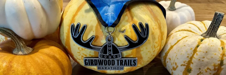 Girdwood Trails Marathon medal with moose antlers over a helmet, resting on white and orange pumpkins.